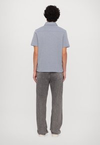 Short-sleeve polo shirt in light blue fabric, featuring a flat collar and straight hem. Worn with gray wide-leg pants, view from the back.