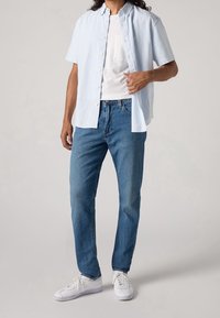 Světle modrá a bílá pruhovaná košile s krátkým rukávem přes bílé tričko, doplněná modrými džíny a bílými teniskami. Ležérní a pohodlný střih.