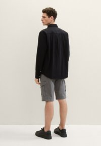 Black long-sleeve shirt with subtle texture, paired with light gray cargo shorts featuring side pockets and black sneakers. Simple, modern design.