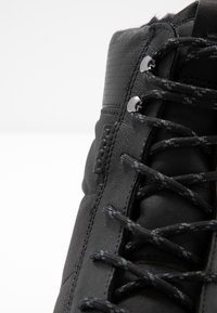 Botte de randonnée noire avec une tige en cuir texturé, des œillets renforcés et des lacets noirs au motif subtil.