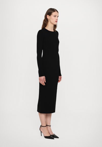 Vestido negro de manga larga con canalé, de silueta recta, con un dobladillo hasta la rodilla y aberturas laterales; combinado con unos tacones negros de puntera afilada y tiras al tobillo.