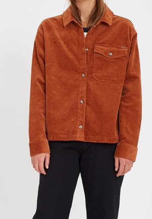 Brown corduroy shirt jacket with a pointed collar, front pocket, and button closure. Features textured fabric and a relaxed fit.