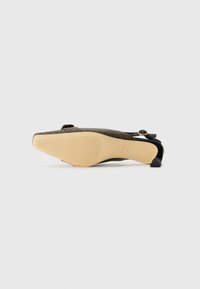 Chaussure pointue noire et marron avec un dessus texturé, une sangle étroite avec une boucle dorée, et un petit talon bloc. Semelle en caoutchouc beige.