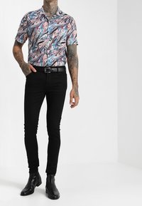 Koszula z krótkim rękawem na guziki z wielokolorowym, abstrakcyjnym nadrukiem; zestawiona z dopasowanymi czarnymi spodniami i czarnymi botkami za kostkę.