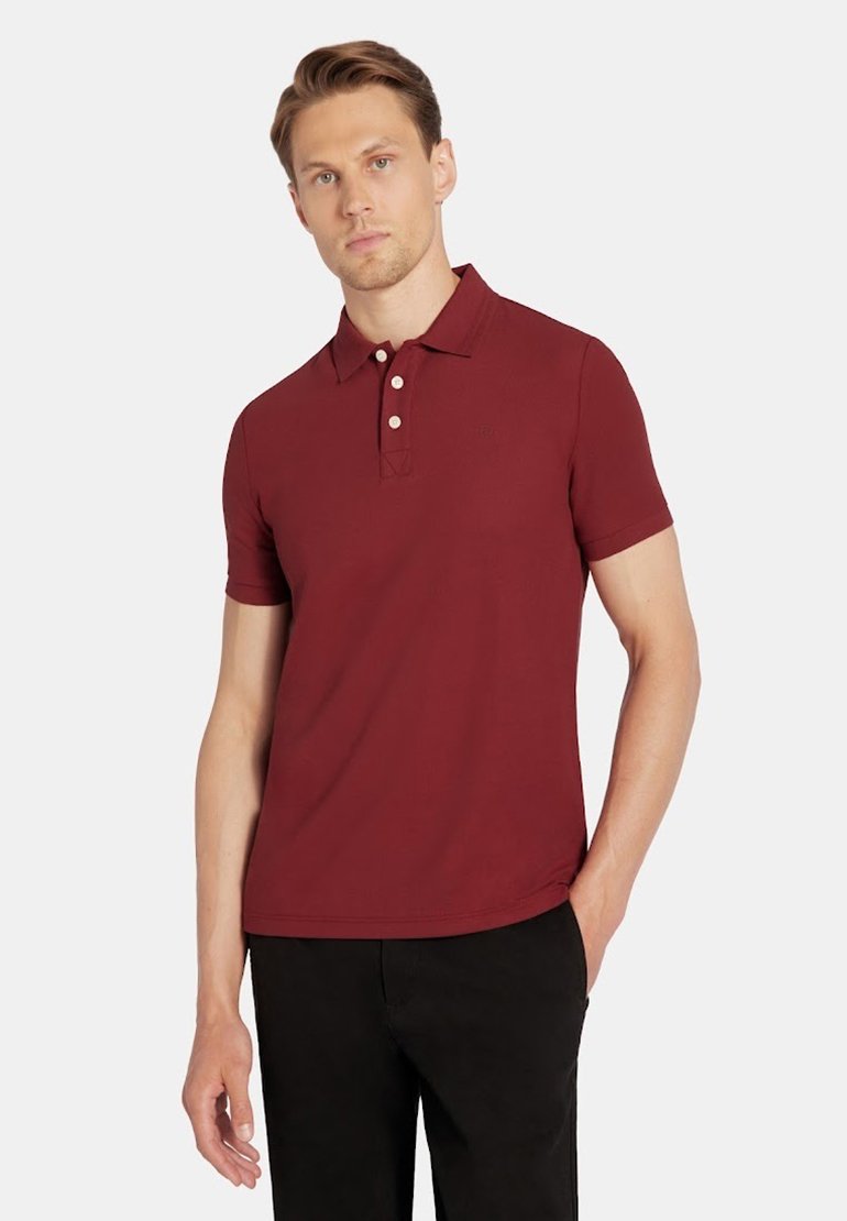 Bordowa koszulka polo z krótkim rękawem, z kołnierzykiem, trzema guzikami oraz subtelną teksturą. Zestawiona z czarnymi spodniami.