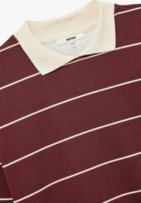 Polo shirt bordeaux con colletto crema, con strisce orizzontali bianche. Realizzato in cotone, ha una consistenza morbida e un design classico.