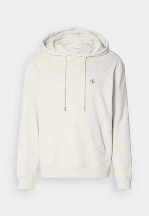 Sudadera con capucha de color beige claro, con un bolsillo tipo canguro, capucha ajustable con cordón, puños acanalados y un pequeño logotipo bordado en el pecho.