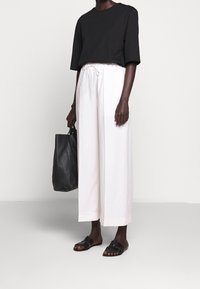 Svart kortärmad topp, vita vida byxor med snörning i midjan, svart läder tote-väska och svarta slidesandaler. Släta texturer, avslappnad design.