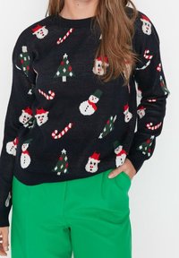 Czarny sweter na drutach z motywami świątecznymi, w tym bałwanki, laski cukrowe i choinki w kolorach czerwonym, zielonym i białym. Z okrągłym dekoltem.