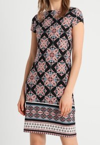 Robe noire à manches courtes présentant un motif floral en losange rose et bleu, avec un ourlet imprimé et une texture lisse.