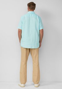 Camicia a maniche corte di colore azzurro chiaro in lino, abbinata a pantaloni beige dalla vestibilità ampia. La camicia presenta un colletto classico e una pence sul retro.