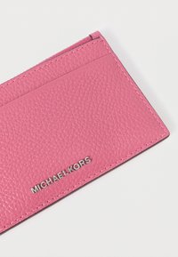 Ροζ δερμάτινη θήκη καρτών με υφή, με ασημένια σήμανση «MICHAEL KORS» στο κάτω μέρος και λεπτομέρειες με ραμμένες ακμές.
