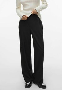 Un pantalon large noir aux textures lisses, avec une taille haute et une silhouette évasée, associé à un haut crème à côtes.