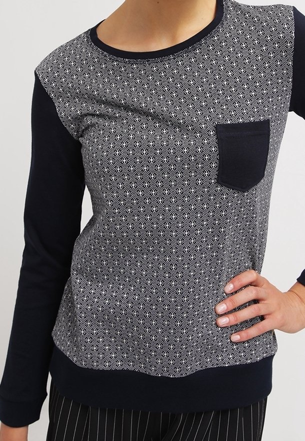 Långärmad topp med en geometrisk mönstrad framsida i grått och vitt, enfärgade marinblå ärmar och en framficka. Mjuk, texturerad tyg.