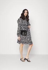 Vestido listrado em preto e branco com detalhes em babados, design com botões, acompanhado de uma bolsa cruzada preta e sandálias de tacão bloco pretas.