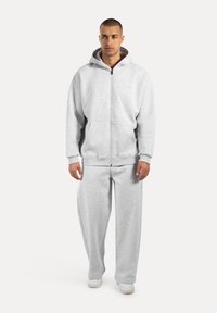 Sudadera gris con cremallera y una capucha amplia, combinada con pantalones grises de corte holgado. Fabricada con un tejido suave y texturizado.