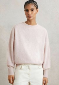 Maglione leggero rosa pallido, soffice, con scollatura rotonda e maniche lunghe leggermente a sbuffo. Abbinato a jeans bianchi per un contrasto delicato.