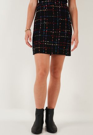 Črna mini krila z večbarvnim tartan vzorcem, strukturirana tkanina in prilagojen silhuet, v kombinaciji s črnimi gležnjarji.