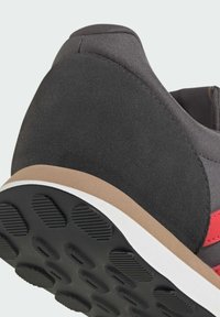 Gros plan sur le talon d'une basket grise et noire avec une semelle noire texturée, une bande médiane beige et un accent latéral rouge.