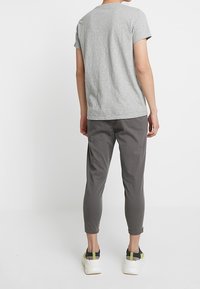 Grå kortärmad t-shirt tillsammans med mörkgrå tapered byxor och vita sneakers med gröna detaljer. Enkelt design och mjuk textur.