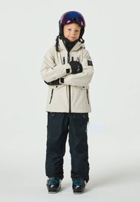 Ski outfit featuring a beige waterproof jacket with black accents, matching black pants, and winter boots with teal details.