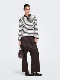 Polo à manches longues rayé en marron et crème, associé à une jupe en satin marron avec bordure en dentelle, et mocassins vernis noirs. Petit sac à main.