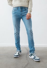 Lyseblå denim jeans med slim fit, der har forlommer og kontraststing. Bæret sammen med blå og hvide sneakers.