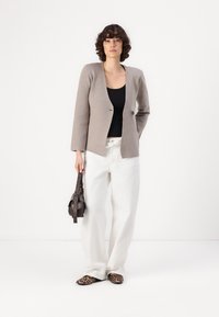 Beige ullblandet blazer med en enkel knapp, kombinert med en svart topp, hvite vide bukser og en brun håndveske. Sko med dyrepprint.