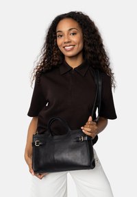 Bolso de mano de cuero negro con asas dobles, correa ajustable y hebillas en tono dorado. Presenta una textura suave y forma rectangular.