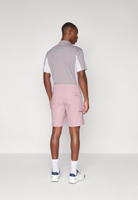 Men's polo shirt in gray and white, paired with light pink shorts. The shorts have side pockets and a smooth texture. White socks and sneakers.