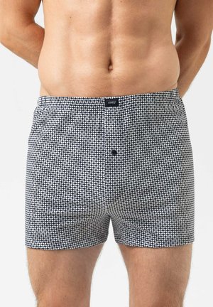 Torso masculin portant un boxer à motif noir et blanc avec une braguette à boutons et une petite étiquette de marque sur la ceinture.