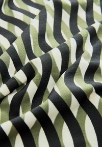 Tessuto a motivi con linee ondulate verdi, nere e bianche; texture morbida e finitura liscia; adatto per diverse applicazioni tessili.