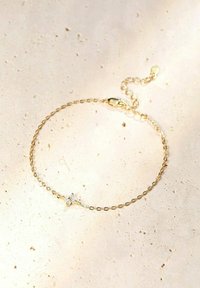 Pulsera de cadena de oro con eslabones ovalados, que presenta un pequeño acento de diamante en el centro. La textura es suave, con un brillo sutil. Longitud ajustable.