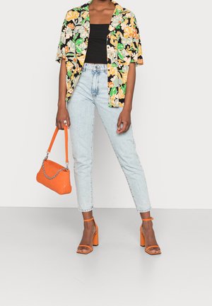 Osoba nosící černý top, květinovou košili s krátkými rukávy, světle modré džíny, oranžové podpatky a držící oranžovou kabelku s řetízkovým detailem.