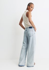 Lichtblauwe wijde denim jeans met een hoge taille en een rafelige zoom; gecombineerd met een lichtgeweven mouwloos topje.
