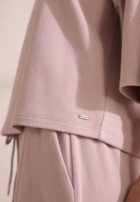 Felpa rosa chiaro con tessuto testurizzato, vestibilità ampia e un'etichetta del brand silver ben visibile etichettata "DOWNTIME" vicino all'orlo.
