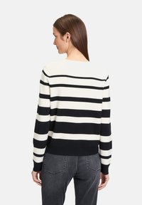 Gestreiftes schwarz-weißes Sweatshirt mit Rundhalsausschnitt, langen Ärmeln und geripptem Saum, kombiniert mit dunkelgrauen Jeans in einer neutralen Umgebung.