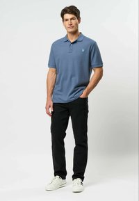 Modrá polo košile s krátkým rukávem, límečkem a malým logem. Kombinováno s černými kalhotami a bílými teniskami. Hladký materiál s přiléhavým střihem.