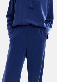 Granatowy zestaw odzieży domowej składający się z topu z długim rękawem z guzikiem i dopasowanych spodni na elastycznym pasku, wykonany z miękkiego, elastycznego materiału.