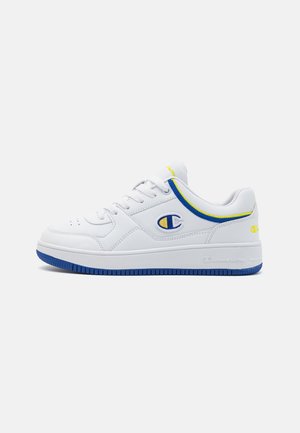 Zapatilla baja blanca de Champion con detalles en azul y amarillo, puntera perforada y suela azul, vista lateral sobre fondo blanco.