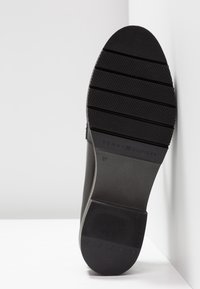 Semelle d'une chaussure noire avec une accroche texturée, des rainures horizontales, taille 37, et le nom de marque "Tommy Hilfiger" gravé près de la voûte plantaire.