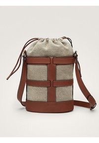 Borsa a secchiello in tessuto beige con cinturini in pelle marrone, base e tracolla regolabile, dotata di chiusura a coulisse nella parte superiore.