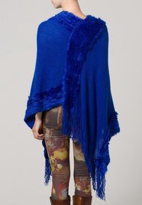 Poncho blu royal con dettagli testurizzati e pelosi ai bordi, con orli frangiati e un design fluido e drappeggiato, che mette in mostra dettagli di stratificazione intricati.