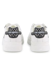 Λευκά αθλητικά παπούτσια με μαύρο υφασμάτινο τακούνι που διαθέτει ασημένια καρφιά και το λογότυπο "Karl Lagerfeld Kids"· καουτσούκ σόλα και κλείσιμο με κορδόνια.