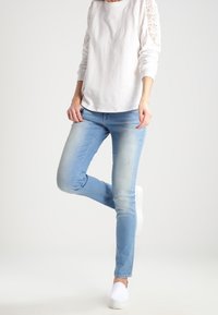 Jeans azzurri chiari con una vestibilità slim, realizzati in denim, abbinati a una camicia bianca a maniche lunghe con dettagli in pizzo sulle maniche.
