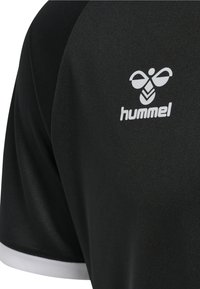 Zwarte sporttrui gemaakt van gladde stof met een wit logo op de linker schouder en een witte afwerking aan de rand van de mouwen.
