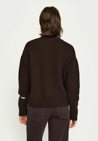 Brun stickad tröja med ribbad nederkant och ärmslut. Har en hög krage och lös passform. Slät textur med en subtil, varm utseende.