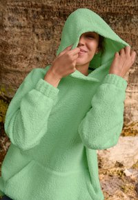 Green fleece hoodie with a textured, soft surface, featuring a large hood, long sleeves, and a front pocket. Casual and cozy design.