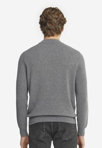 Grauer Rundhalsausschnitt-Pullover aus weichem Strickmaterial, mit langen Ärmeln und ribbeltenden Saum, kombiniert mit dunklen Jeans.