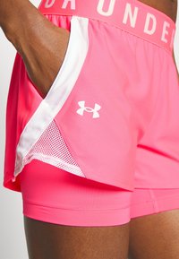 Pantalones cortos deportivos rosas con un panel lateral de malla blanca y una cinturilla elástica ancha con el texto "UNDER ARMOUR." Logo blanco en la pierna.